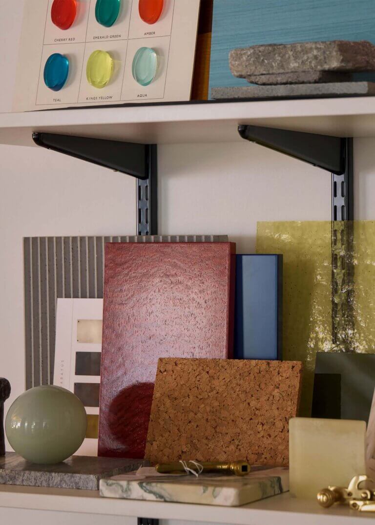 Branding and identity image for Waldo Studio featuring a curated display shelf of architectural and interior material samples, including colour studies, wood, stone, cork, glass, and textured finish panels arranged in a studio setting.